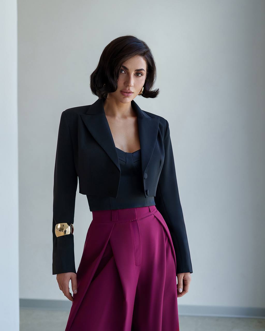 Woman wearing a black blazer and magenta skirt against a plain background
