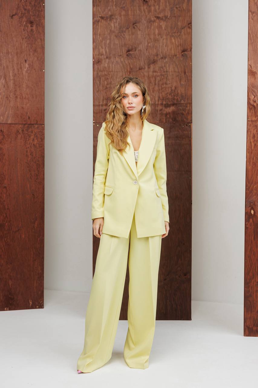 Woman wearing a light yellow suit standing against a wooden panel background