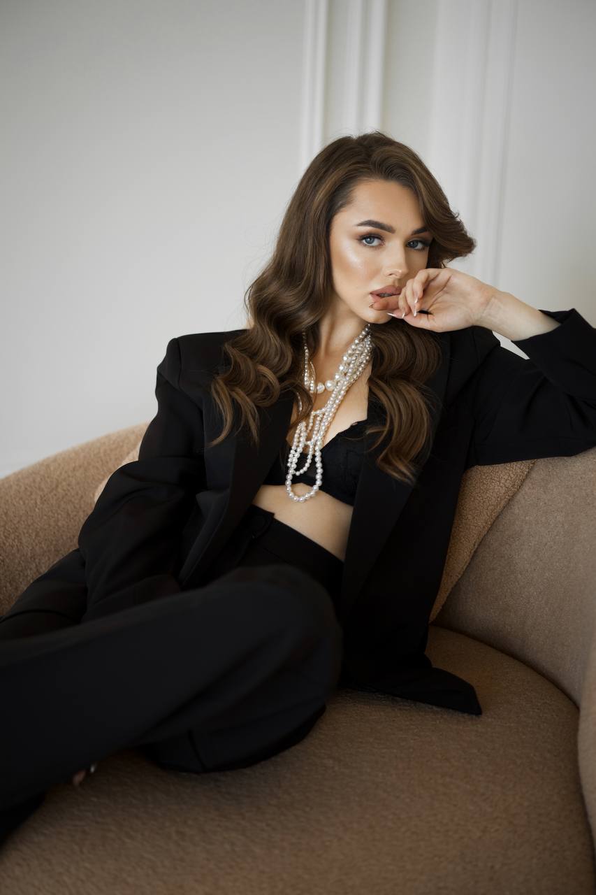 Woman in a black outfit with pearl necklace sitting on a beige couch.