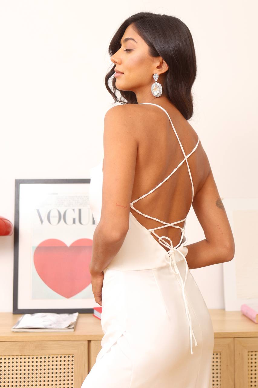 Woman wearing a white dress with thin straps in front of a Vogue magazine cover.