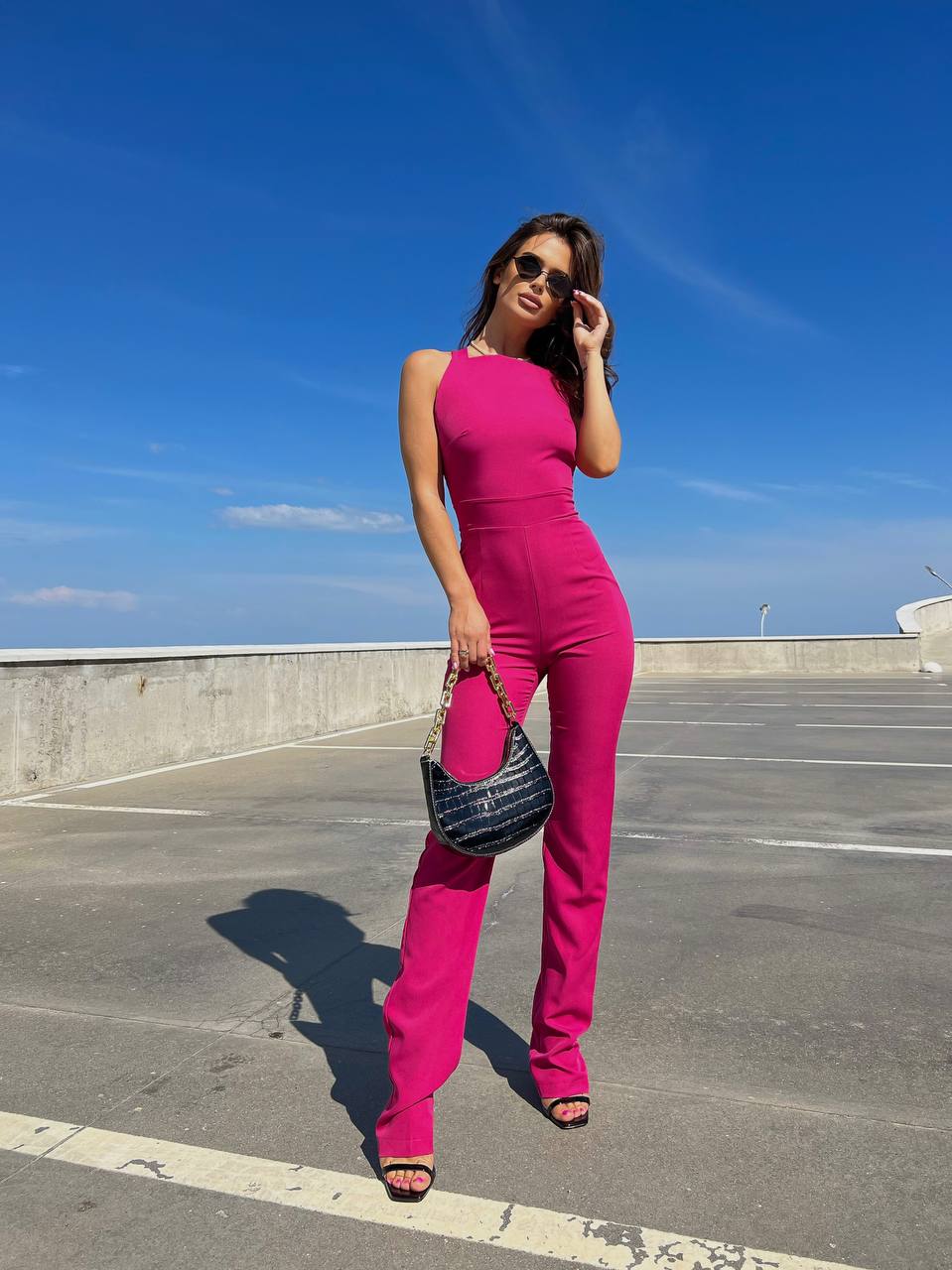 Woman in a bright pink jumpsuit standing on a rooftop with a clear blue sky.