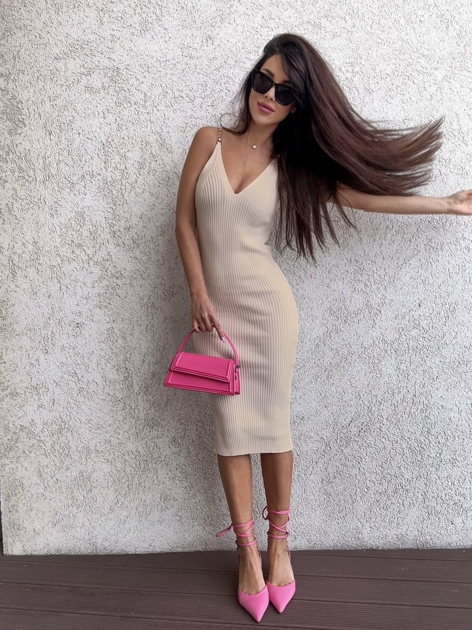 Woman in a beige dress with a pink handbag against a textured wall.