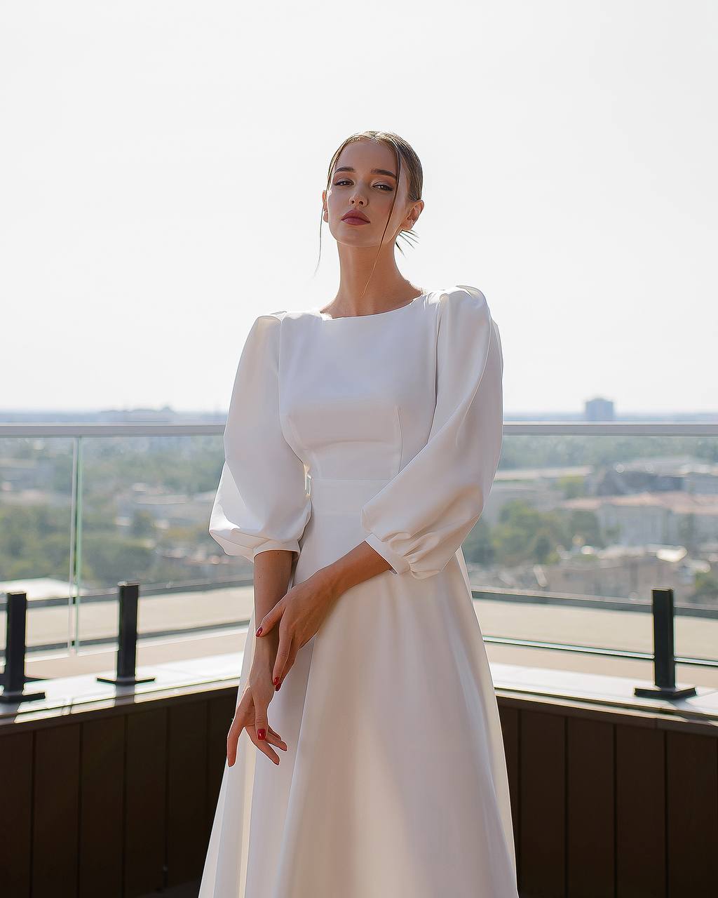 Woman in a white dress standing on a balcony with a cityscape view.
