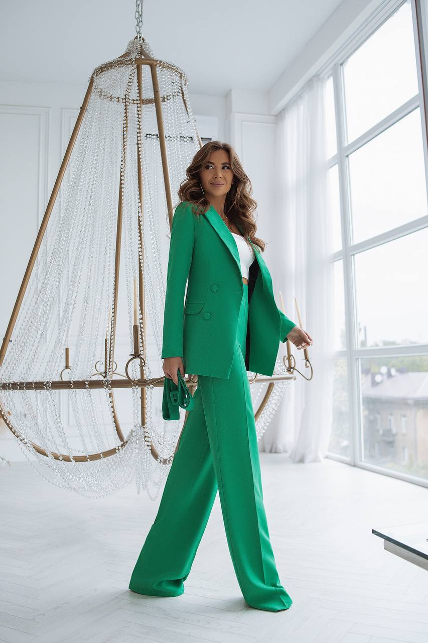 Woman in a green suit standing in a bright room with large windows.
