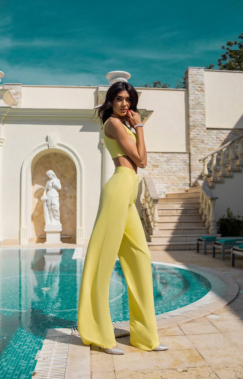 Woman in a yellow outfit standing by a pool with classical architecture in the background