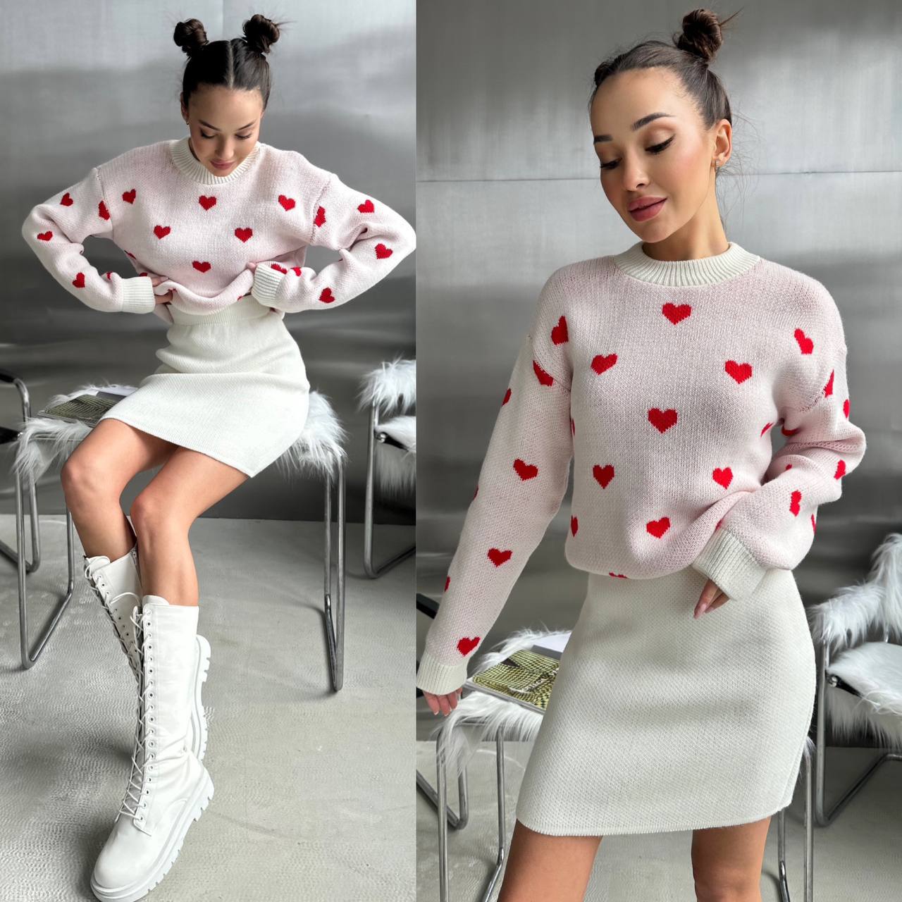 Woman wearing a pink sweater with red heart patterns and a white skirt in a room.
