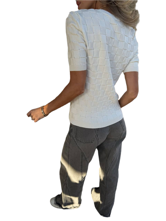 Person wearing a textured white top and dark pants on a white background