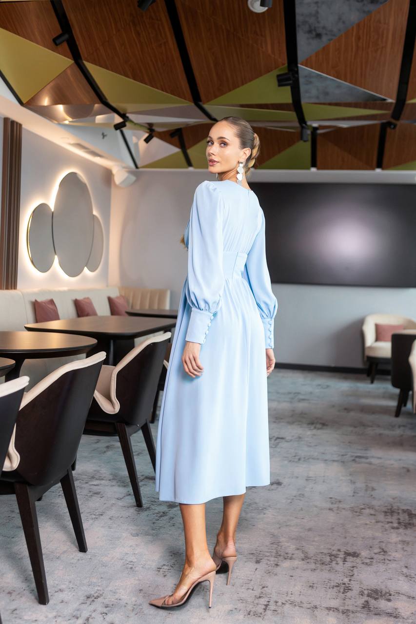 Woman in a light blue dress standing in a modern restaurant with geometric ceiling design.
