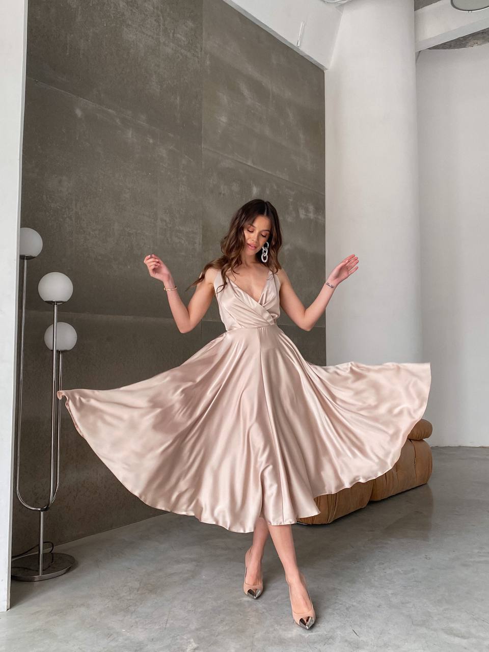 Woman in a beige dress twirling in a modern room with gray walls and a white column.