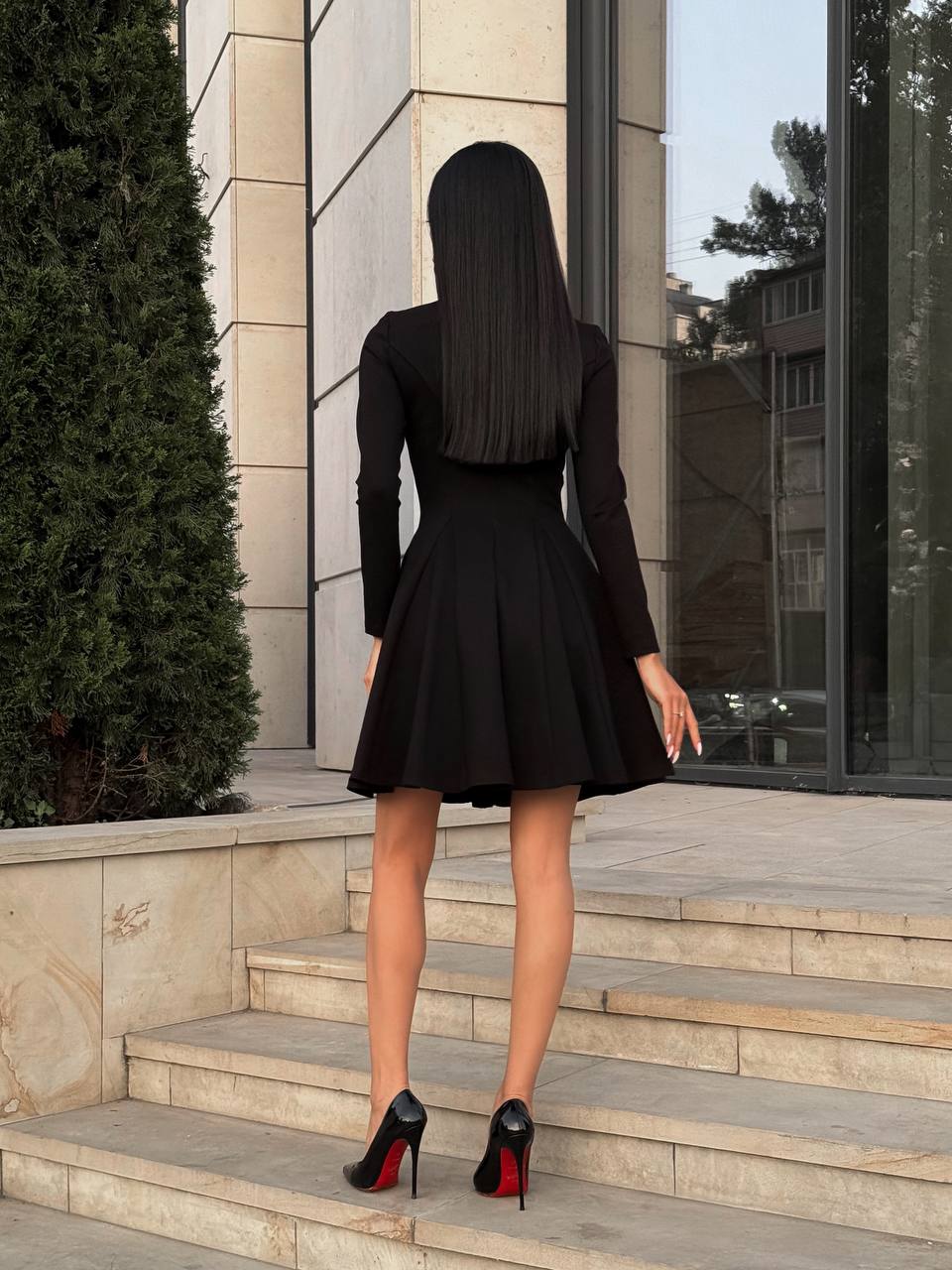 Person wearing a black dress and high heels standing on steps outside a building.
