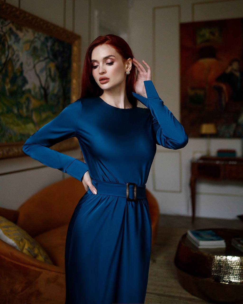 Woman in a blue dress standing in a room with paintings on the wall.