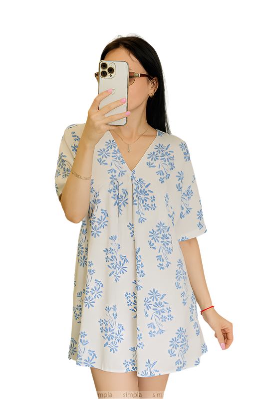 Woman wearing a floral dress taking a mirror selfie on a white background