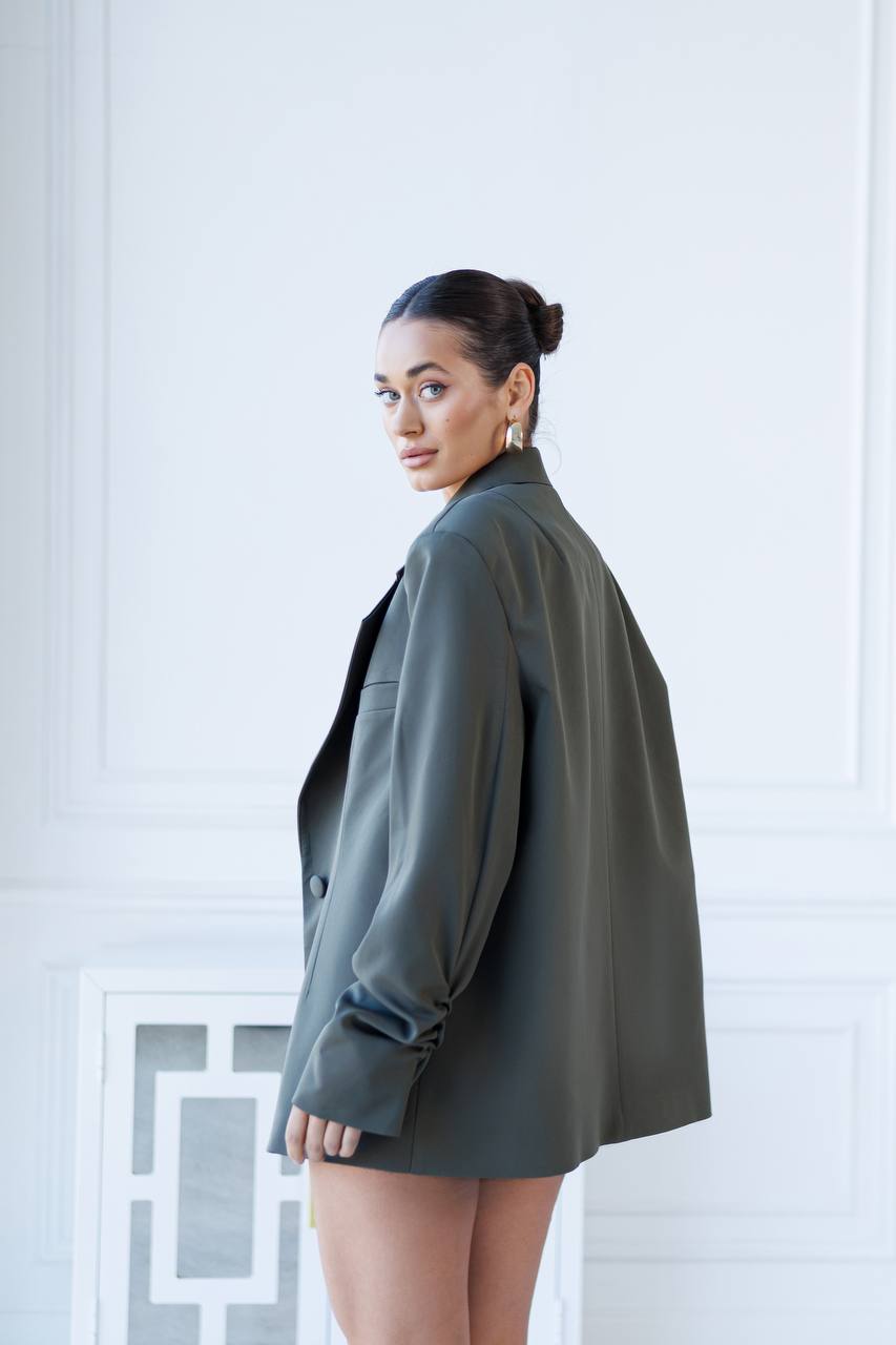 Woman wearing a green blazer over a black top against a white wall.