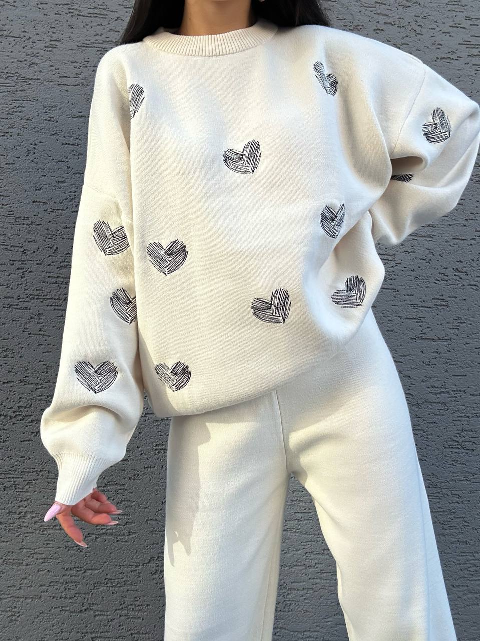 White sweater with heart patterns worn by a person against a gray background