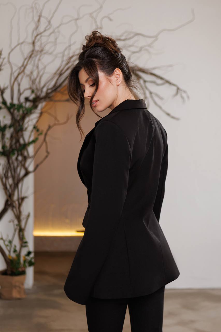 Woman wearing a black outfit in a minimalistic indoor setting with plants.