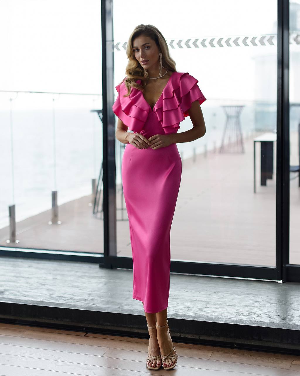 Woman wearing a pink dress with ruffled sleeves in an indoor setting.