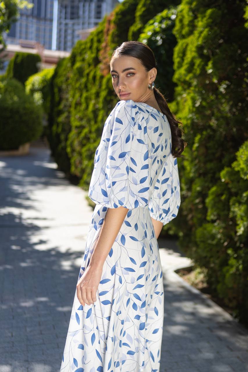 Woman in a white dress with blue leaf pattern walking outdoors.