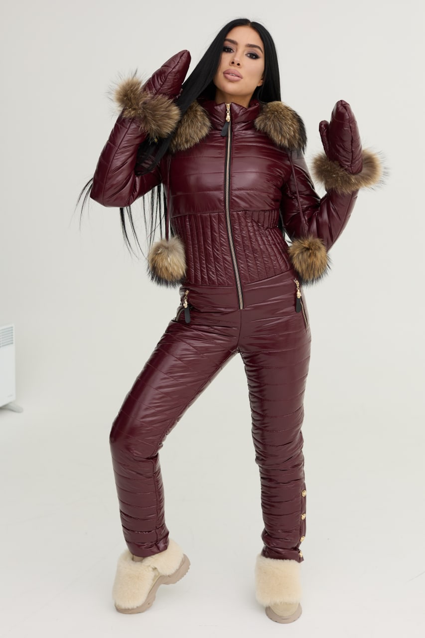 Woman wearing a burgundy quilted jumpsuit with fur trim on a white background
