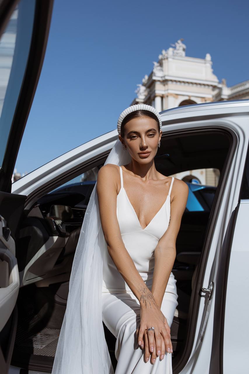 Woman in a white wedding dress sitting in a car with a cityscape in the background