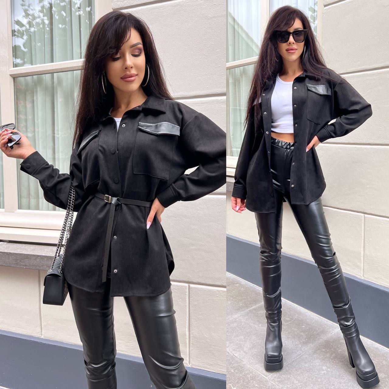 Woman in black outfit with leather pants and jacket standing outdoors.
