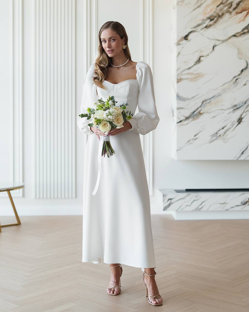 Woman in a white wedding dress holding a bouquet in a modern interior setting