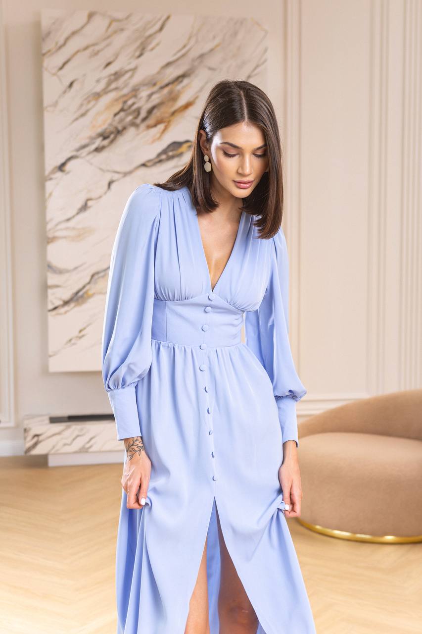 Woman wearing a light blue dress in an indoor setting with a marble wall.