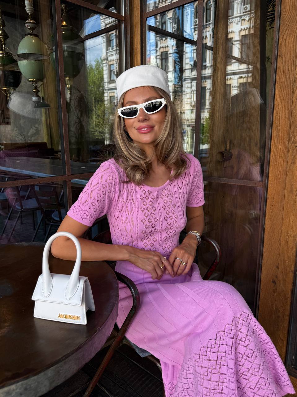 Woman in a pink dress sitting at a table with a white handbag in a cafe.