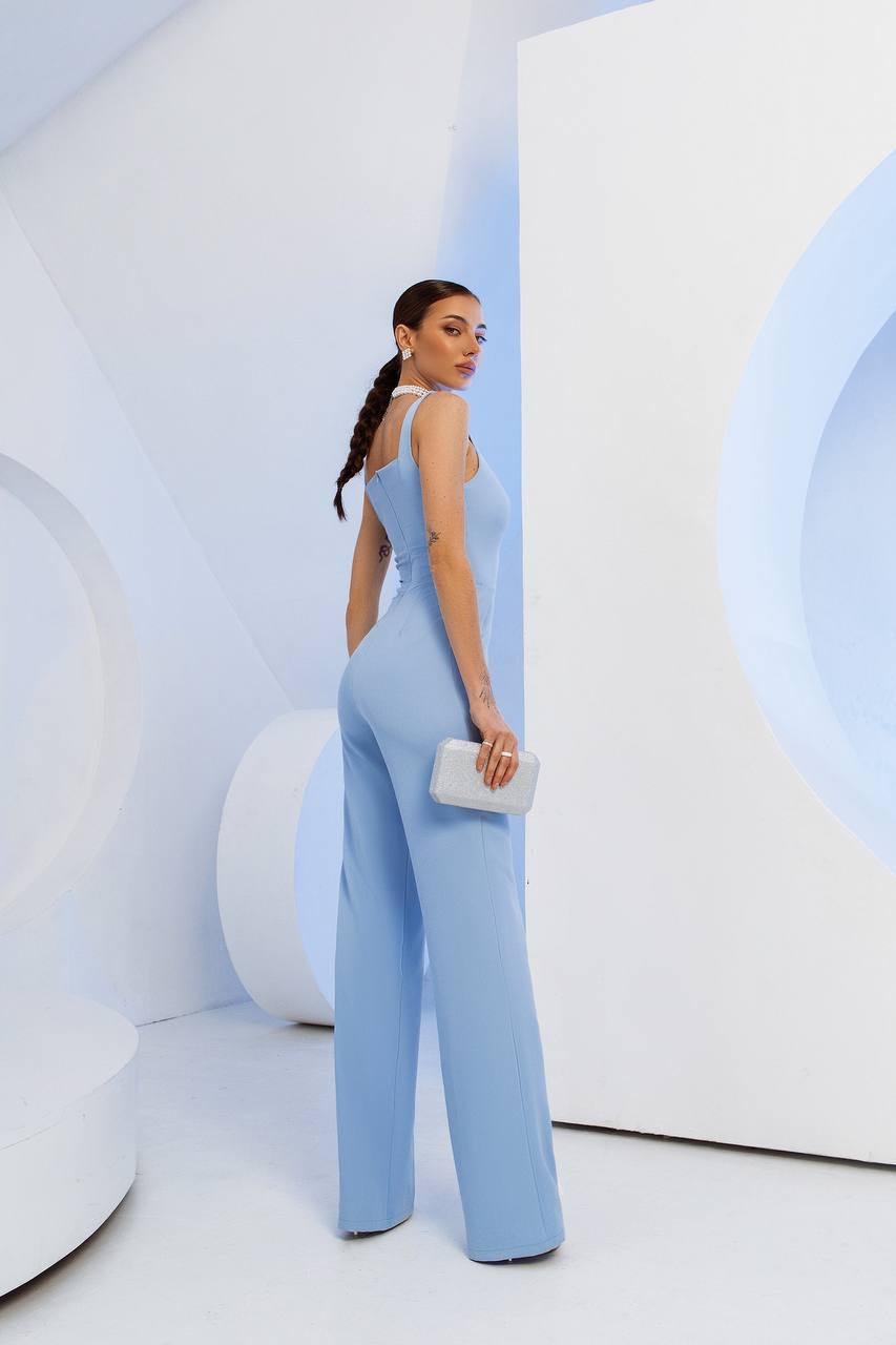 Woman in a light blue jumpsuit standing against a white abstract background