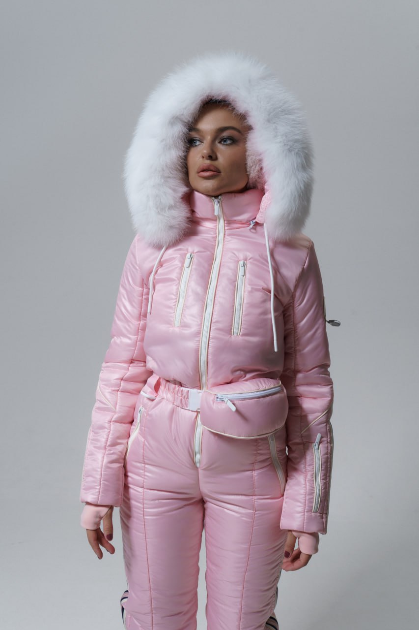 Person wearing a pink puffer suit with a white fur hood on a gray background