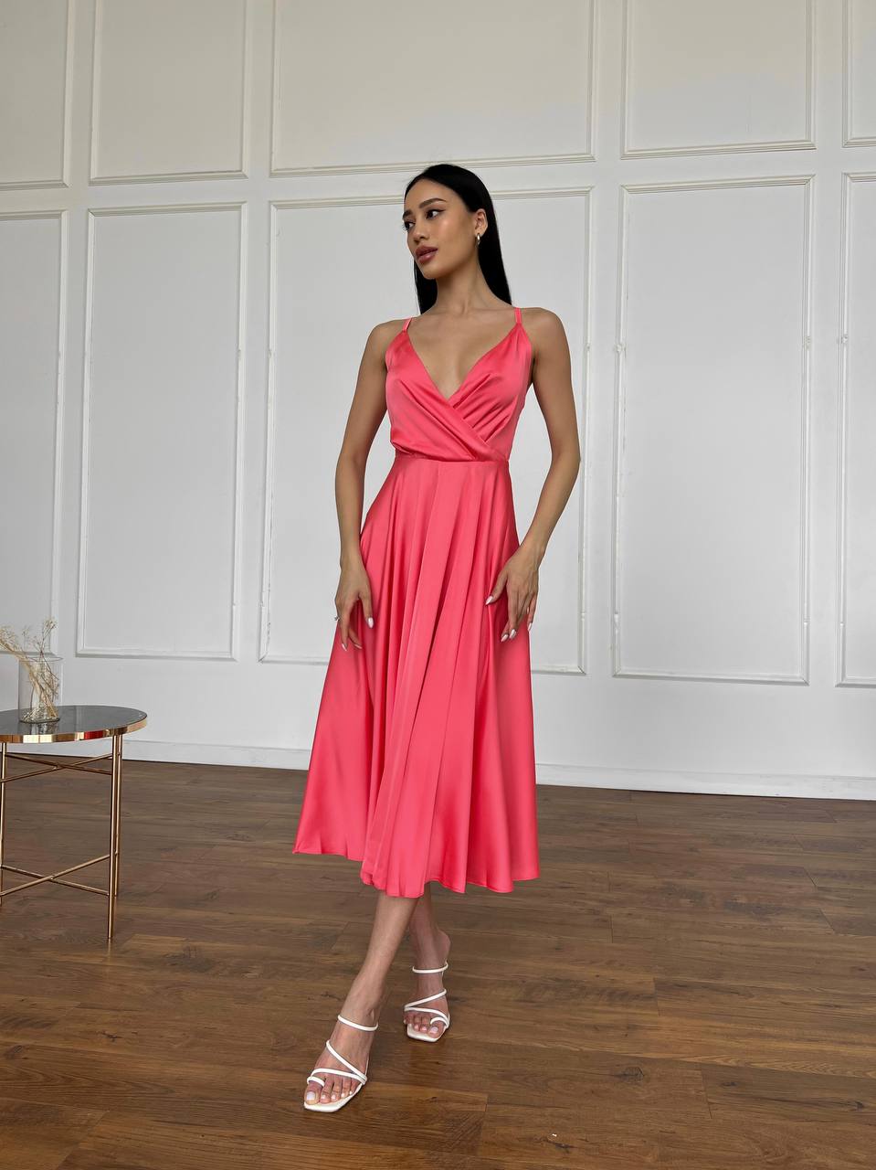 Woman in a pink dress standing in a room with wooden flooring and white paneled walls.