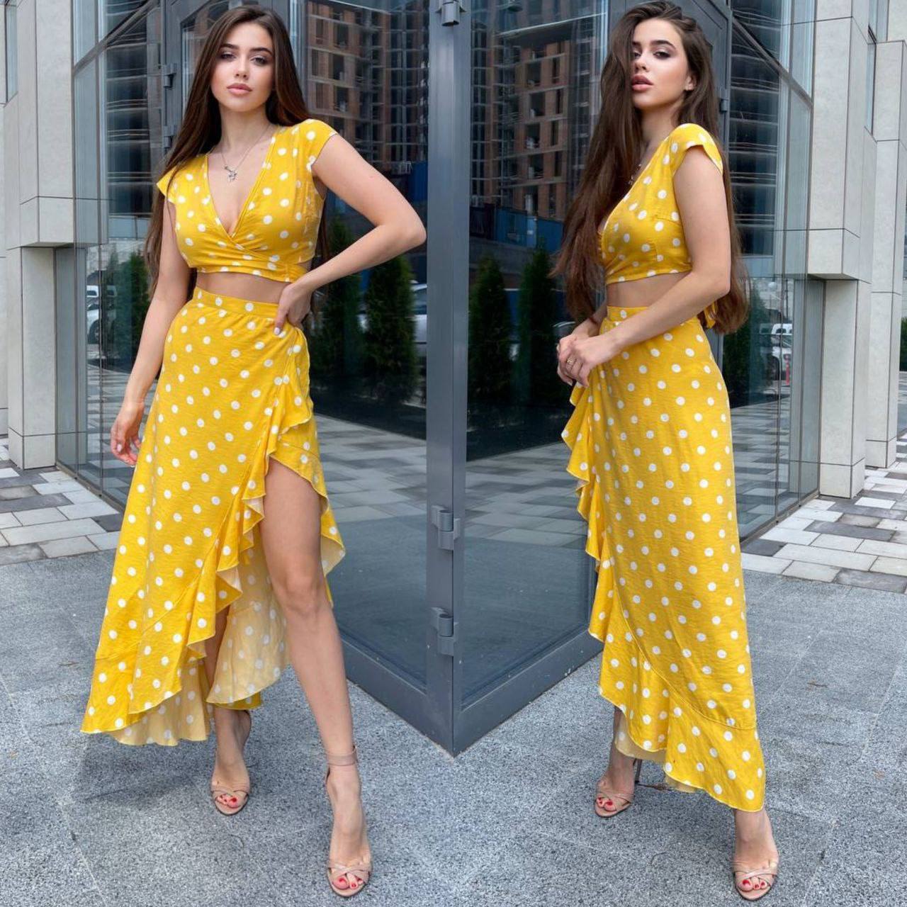 Woman in a yellow polka dot dress standing in front of a glass door.