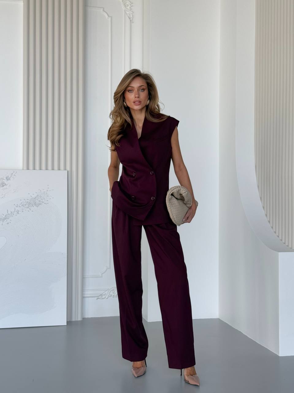 Woman in a burgundy jumpsuit standing in a minimalistic room with white walls.