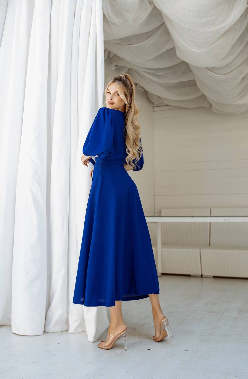 Woman in a blue dress standing in a room with white curtains and ceiling.
