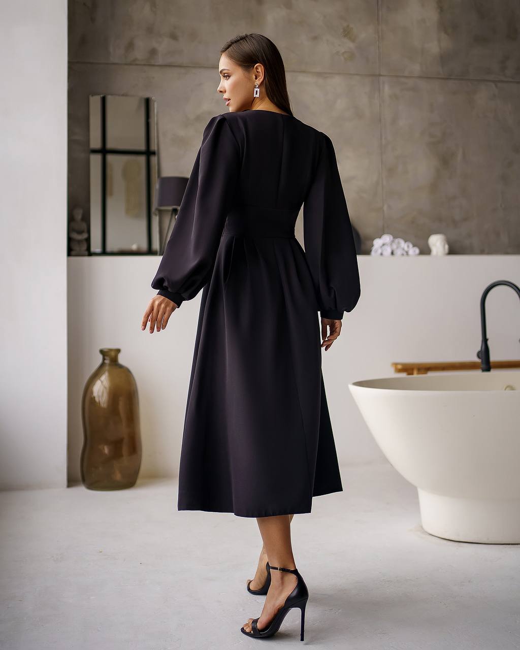 Woman in a black dress standing in a modern bathroom.