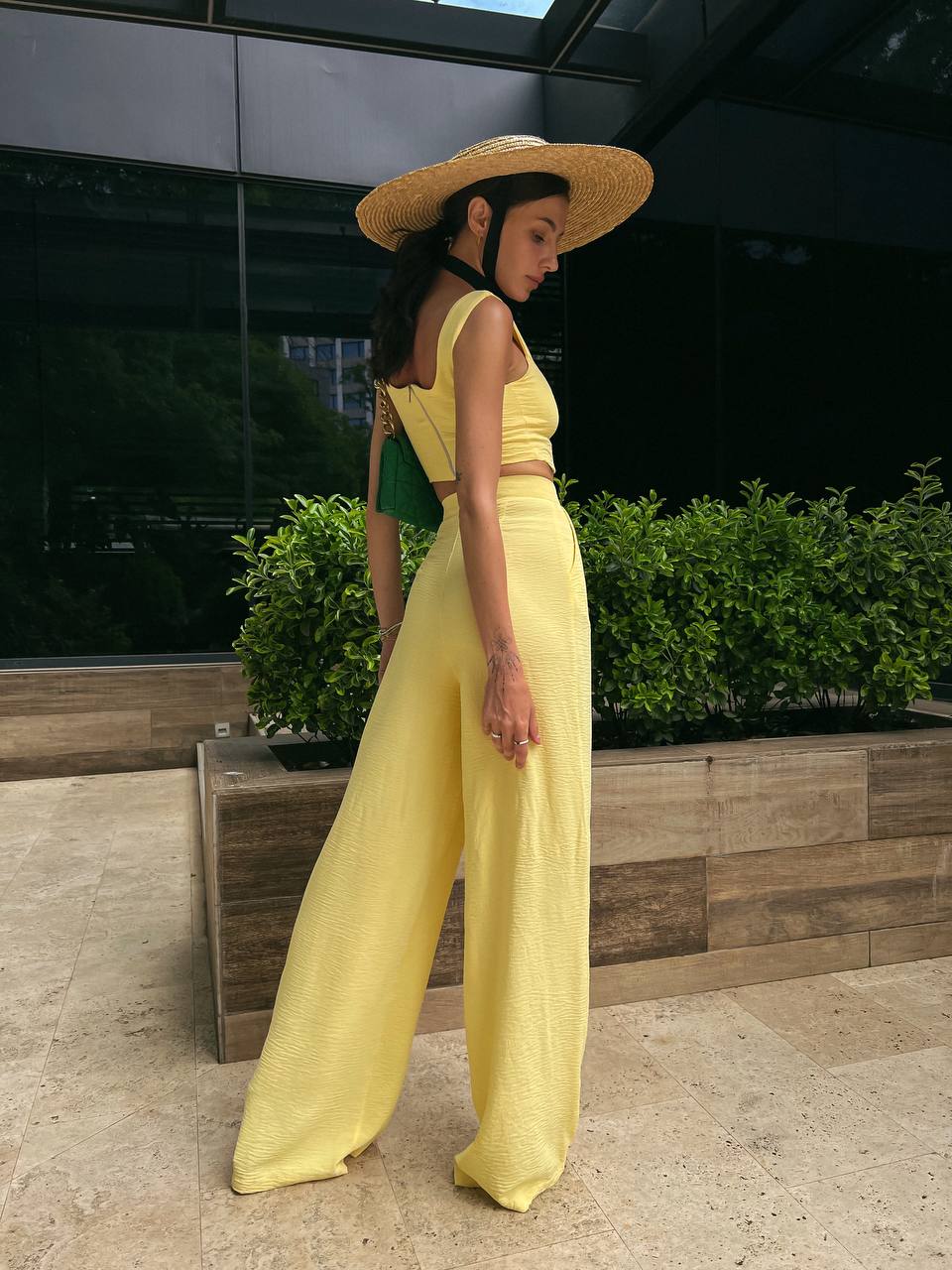 Woman in a yellow outfit and straw hat standing outdoors.