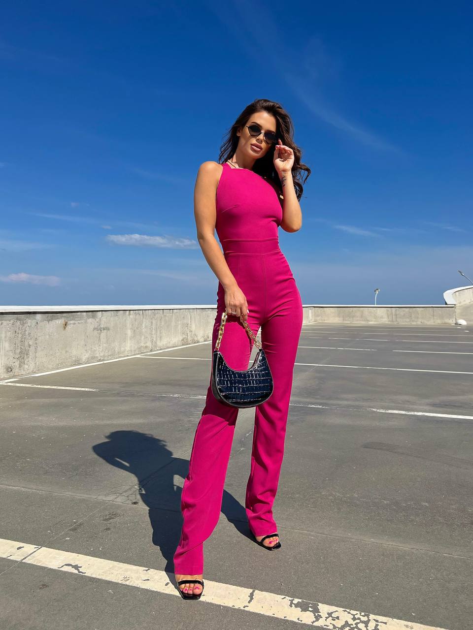 Woman in a bright pink outfit standing on a rooftop with a clear blue sky.