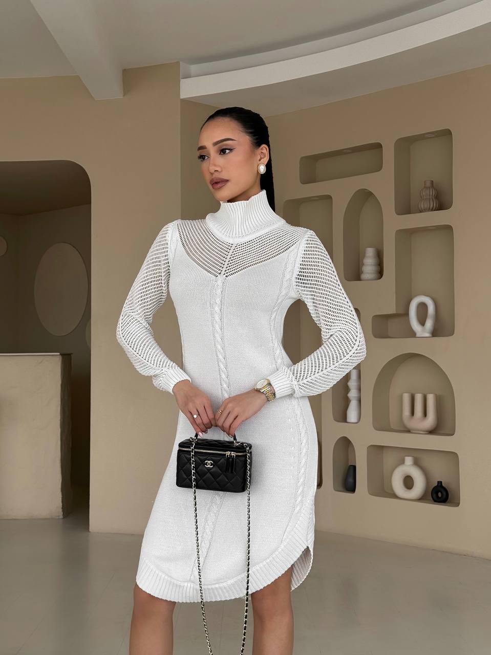 Woman in a white dress holding a black handbag in a modern interior setting