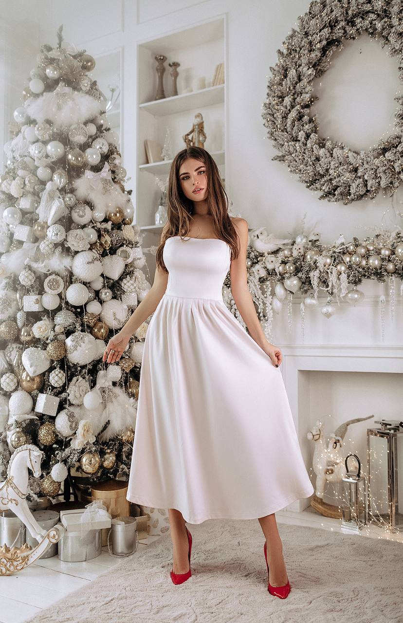 Woman in a white dress standing in a decorated room with Christmas trees and wreaths.