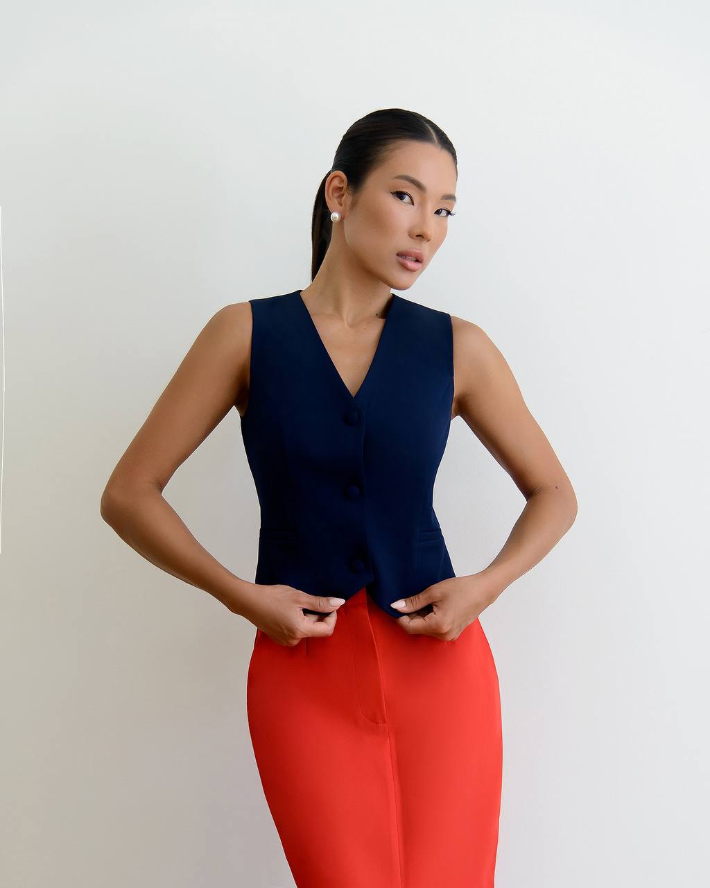 Woman wearing a navy sleeveless top and red pants against a white background
