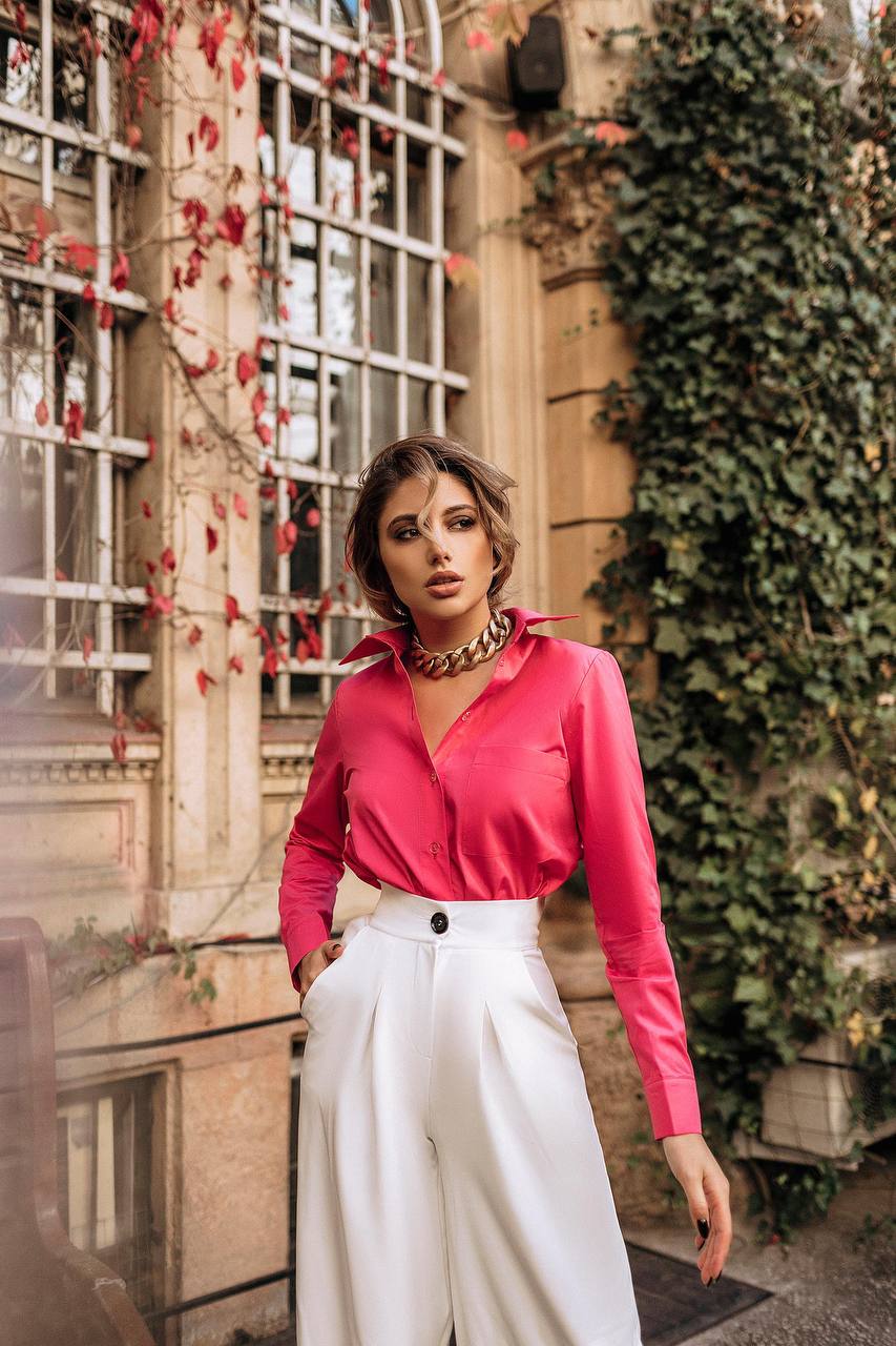 Woman wearing a pink blouse and white pants standing in an outdoor setting with ivy and red leaves.