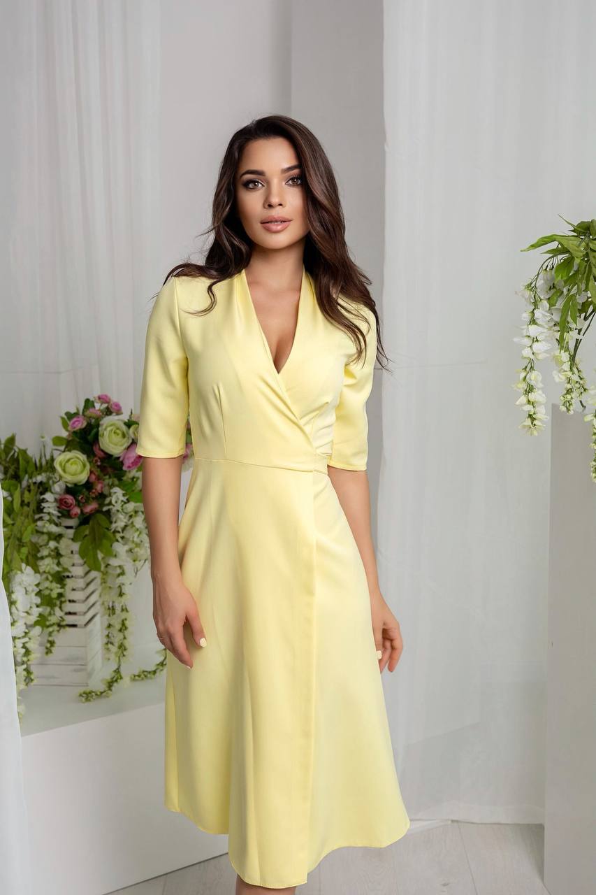 Woman wearing a yellow dress with a matching jacket in a minimalistic setting with plants.