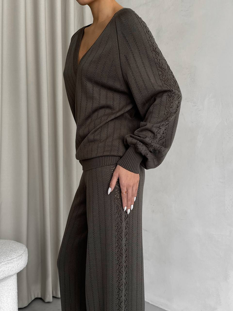 Person wearing a brown ribbed sweater and pants against a neutral background