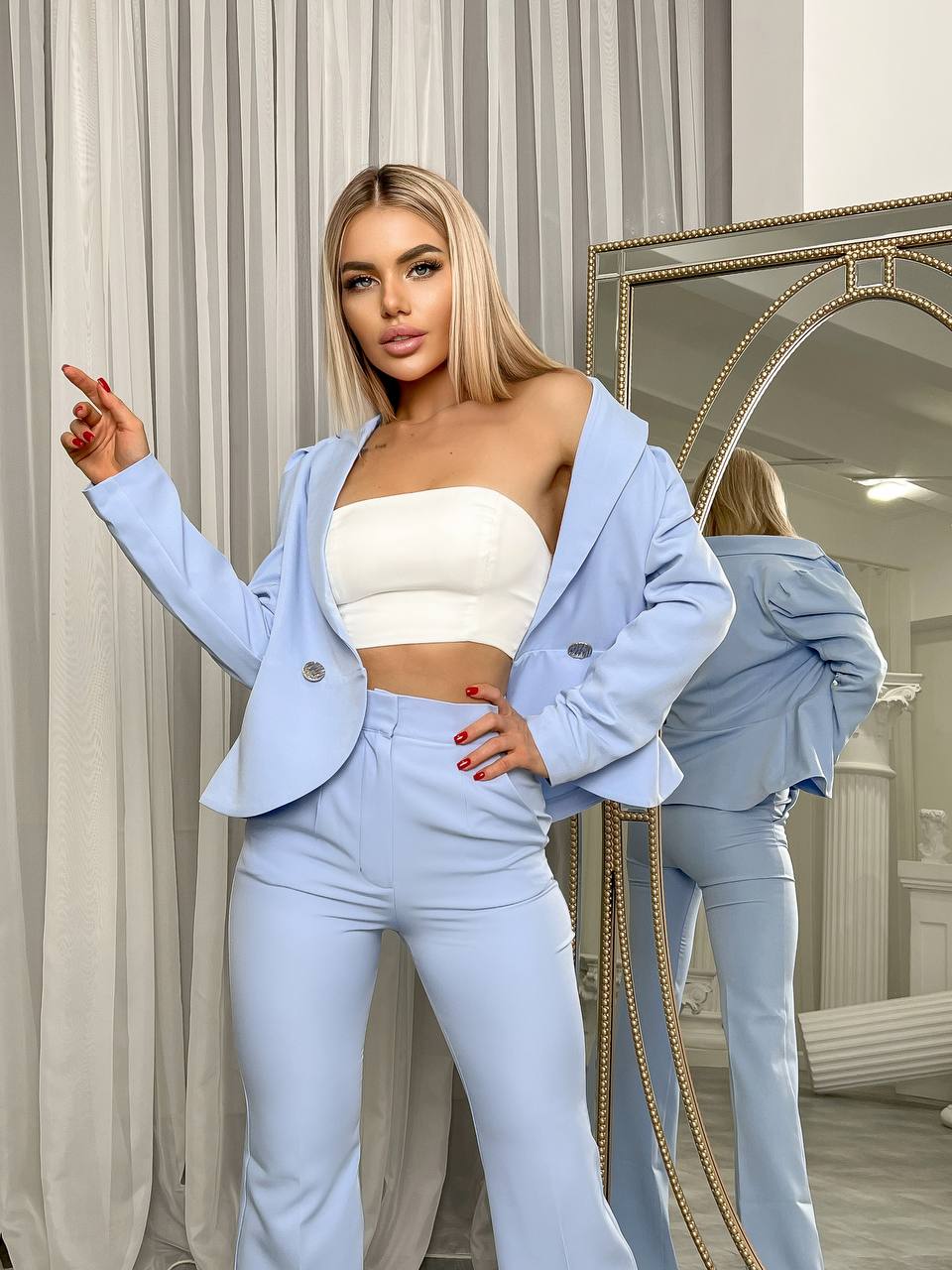 Woman in light blue blazer and pants posing in front of a mirror.