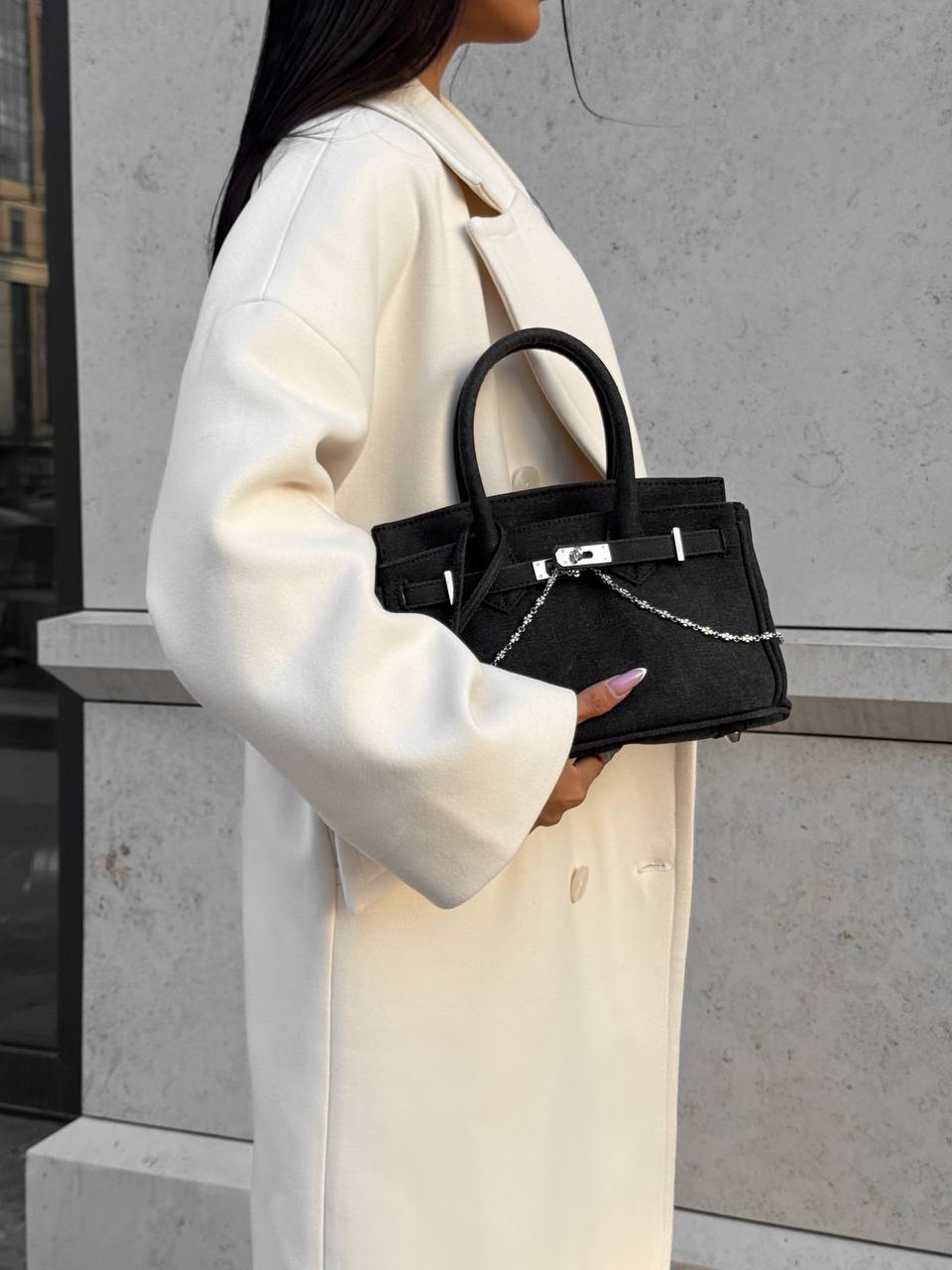 Person holding a black handbag against a neutral background