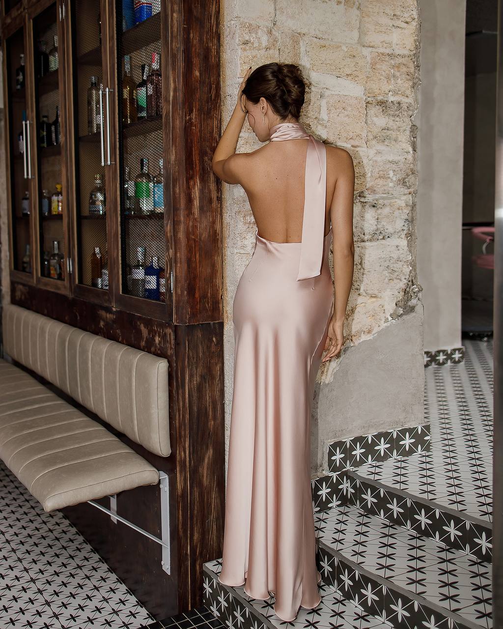 Woman in a long pink dress standing near a bar with a stone wall background
