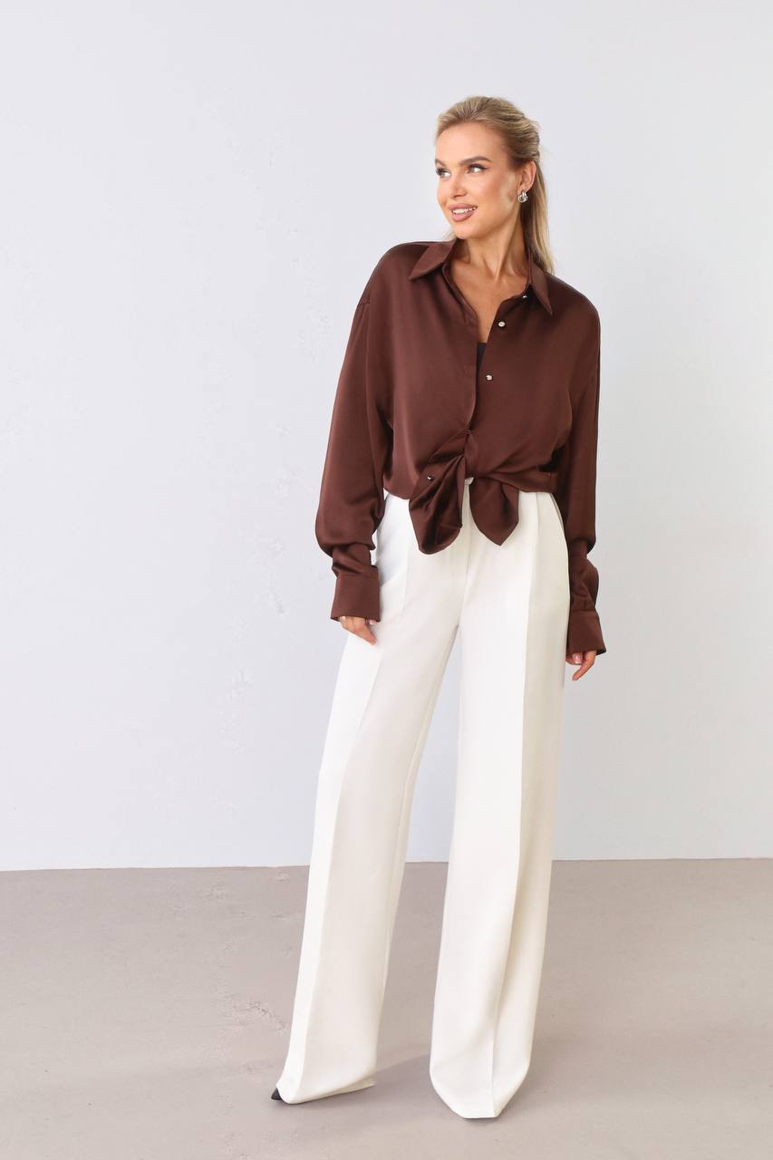 Woman wearing a brown blouse and white pants against a plain background