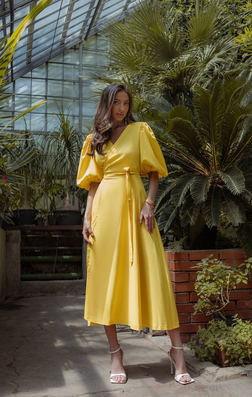 Woman in a yellow dress standing in a greenhouse with plants around