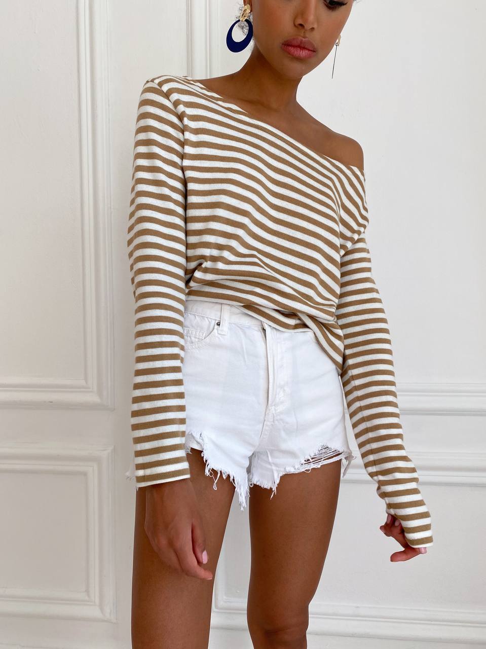 Person wearing a striped long-sleeve top and white shorts against a white wall.