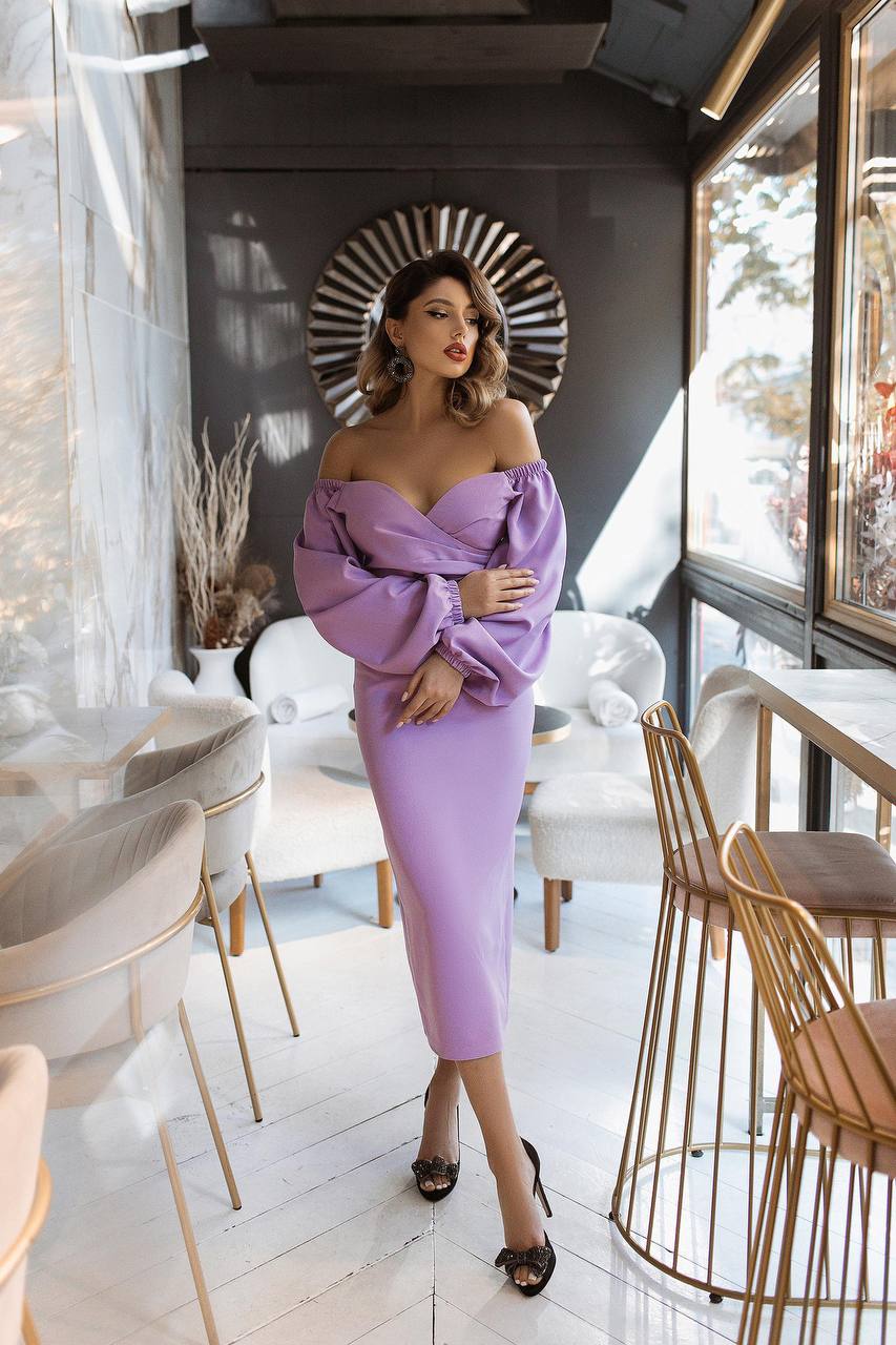 Woman in a purple dress standing in a modern interior setting with tables and chairs.