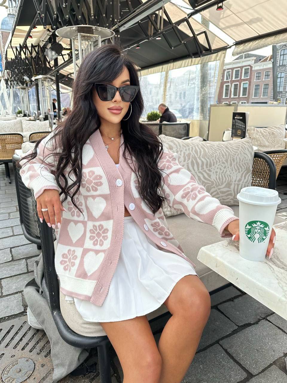 Woman in a pink cardigan and white dress holding a Starbucks cup outdoors.